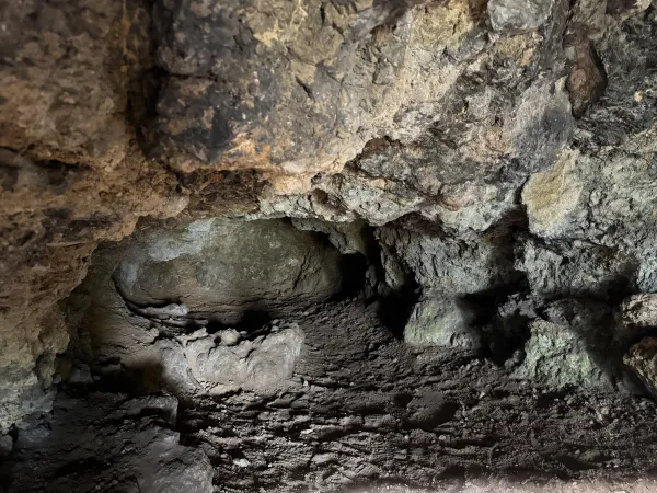 Der Blick in eine dunkle Höhle mit unebenem, erdigem Boden und zerklüfteten Felswänden am Staffelberg. Die raue Gesteinsoberfläche zeigt natürliche Vorsprünge und eine dunkle Öffnung im Hintergrund. (KI-generierte Bildbeschreibung)