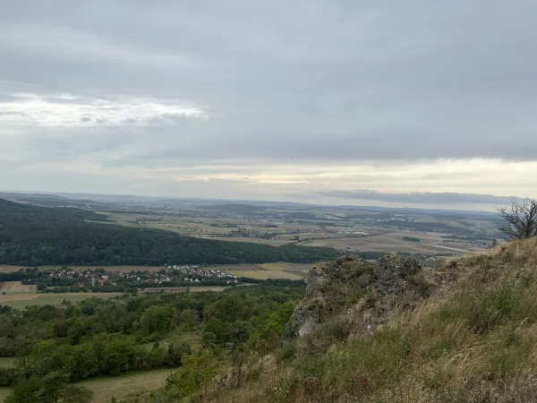 Blick vom felsigen Plateau des Staffelbergs über eine weite Landschaft mit Feldern, Wäldern und kleinen Ortschaften unter einem bewölkten Himmel. (KI-generierte Bildbeschreibung)
