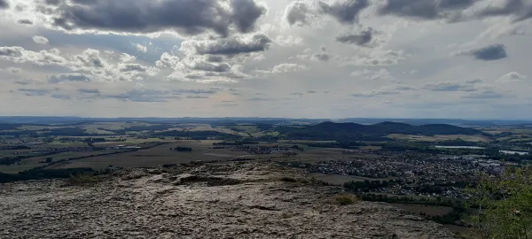Weitblick vom felsigen Plateau des Staffelbergs über die umliegende Landschaft mit Feldern, Wäldern und Ortschaften unter einem bewölkten Himmel. (KI-generierte Bildbeschreibung)