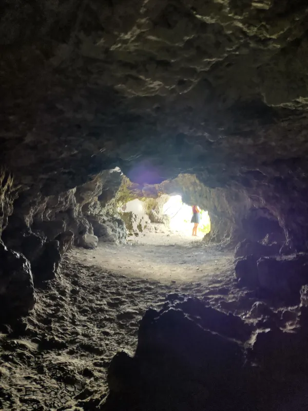 Blick aus dem dunklen, felsigen Inneren einer Höhle auf den tageslichtdurchfluteten Ausgang, an dem eine Person steht. (KI-generierte Bildbeschreibung)